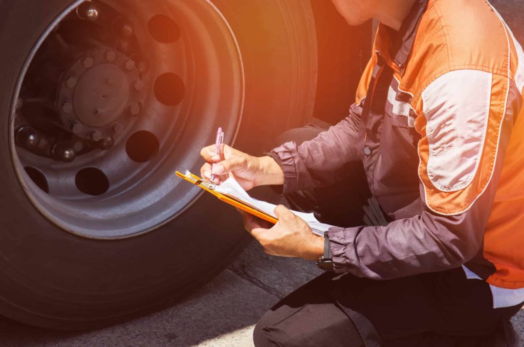 Person looking at a car tire while writing on a clipboard