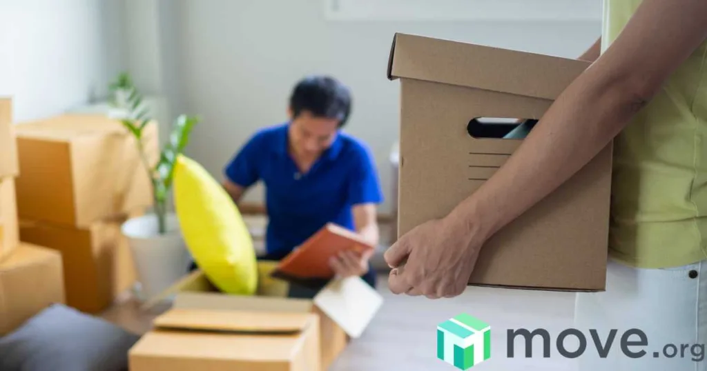Arms holding a moving box in front of a man unpacking a box