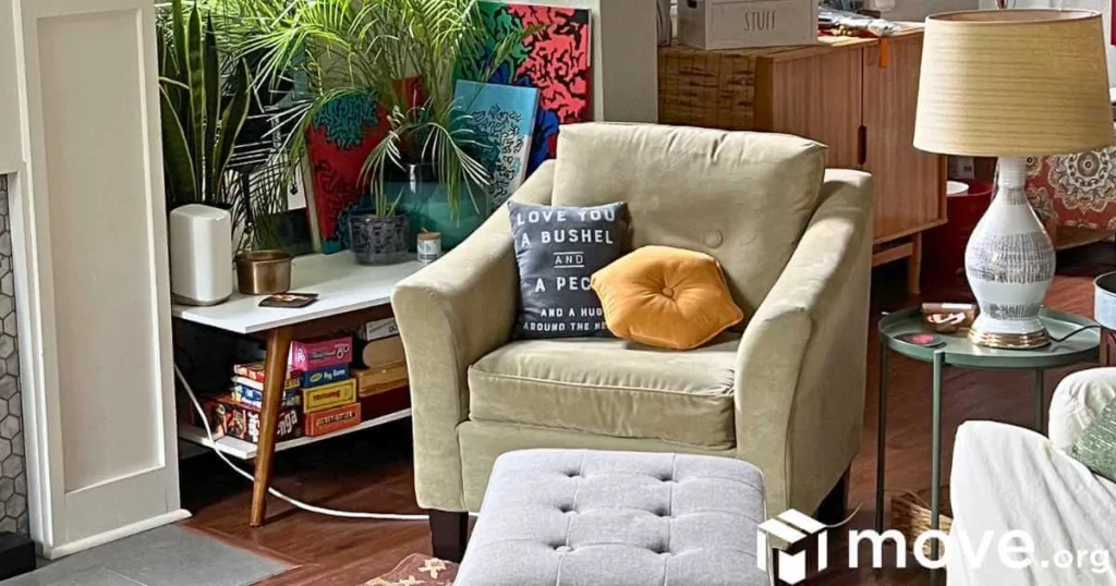 A cozy reading nook with a soft, green chair, pillows, nearby lamp, ottoman, and plants.