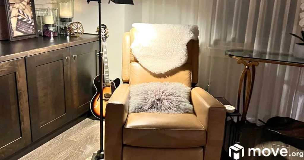 A leather recliner with a fleece throw and fluffy pillow, illuminated by a floorlamp, with a guitar in the background. A perfect cozy reading nook.