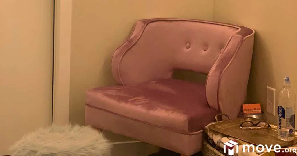 A velvet chair in a corner with a fluffy white ottoman and a side table - ready for reading and coziness.