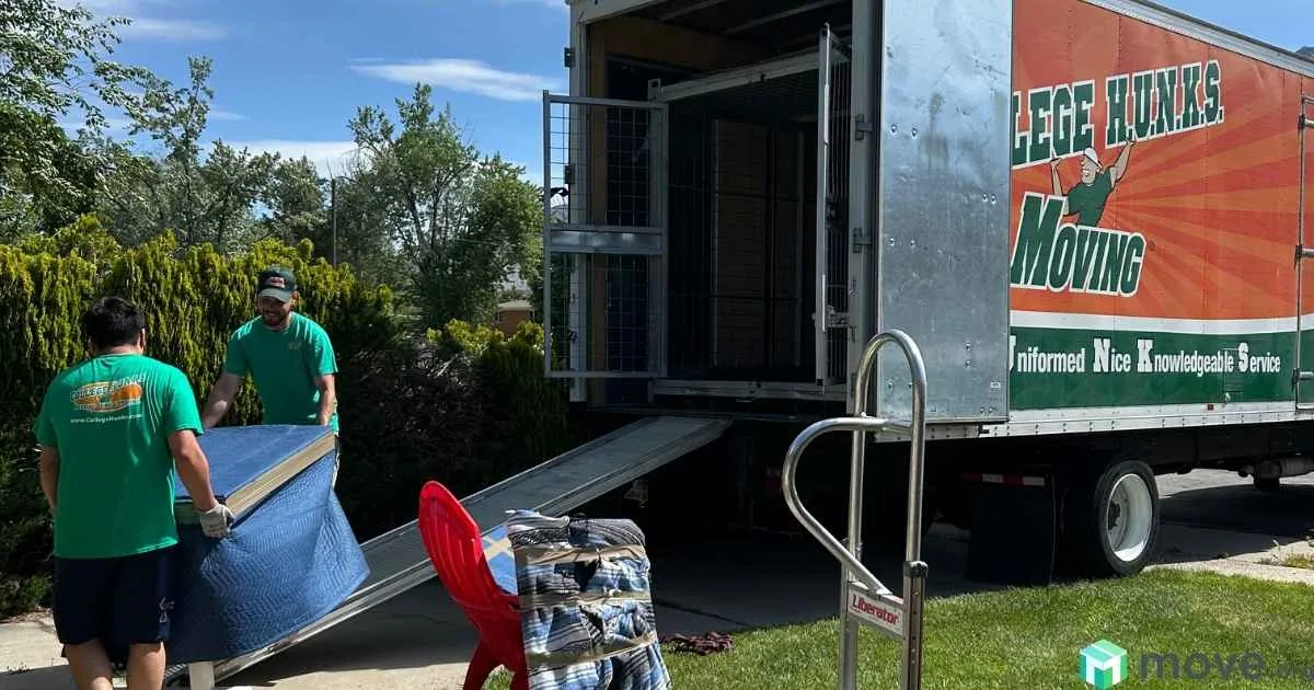 Two movers loading a piece of furniture into a Zippy Shell moving container, using a ramp to walk up to the back of the truck.